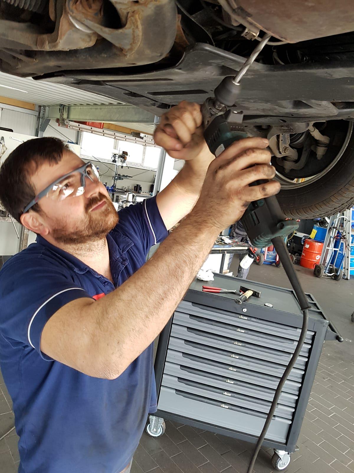 Mechaniker mit Schutzbrille arbeitet mit Werkzeug unter einem angehobenen Fahrzeug