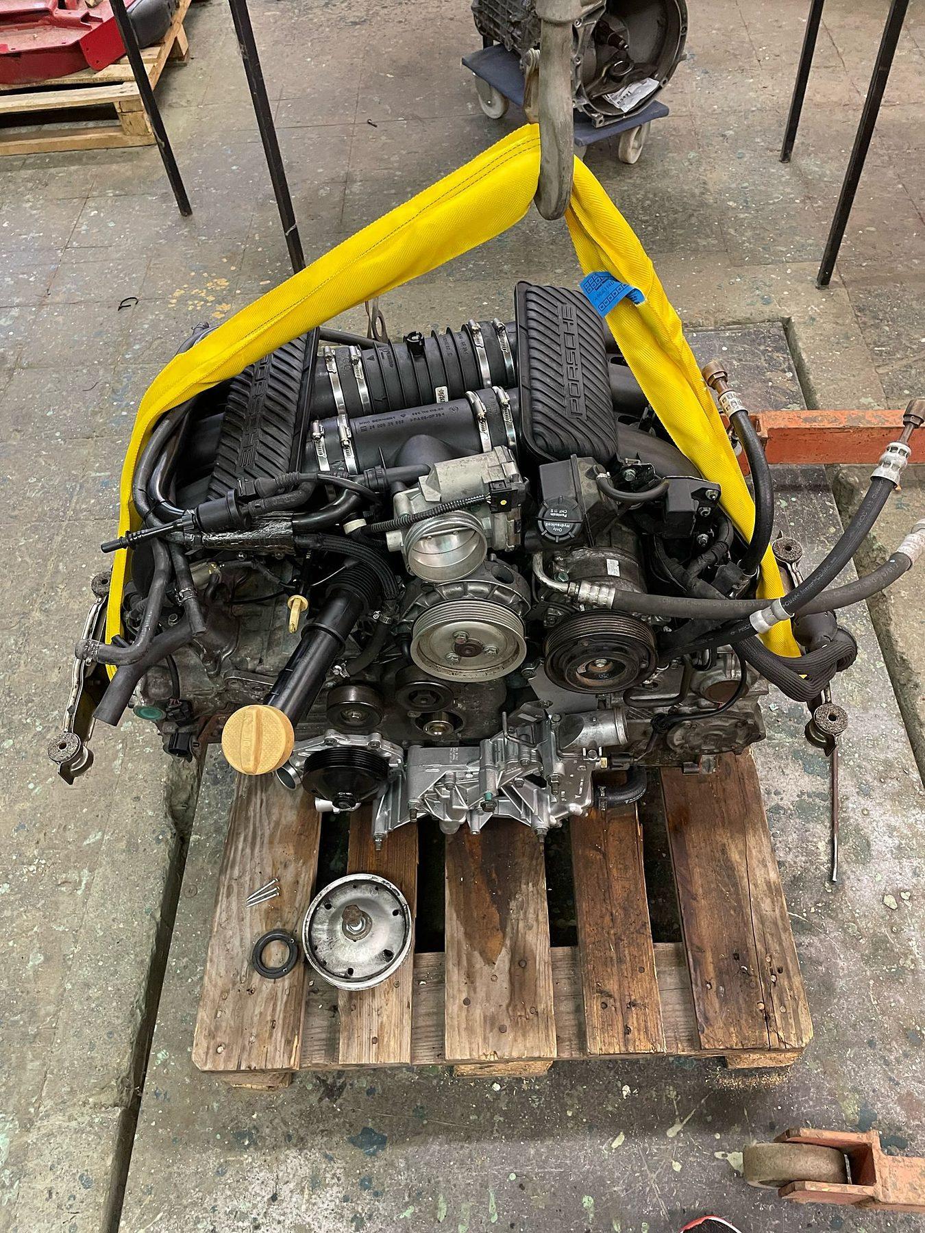 Boxermotor hängt am gelben Hebegurt über einer Palette
