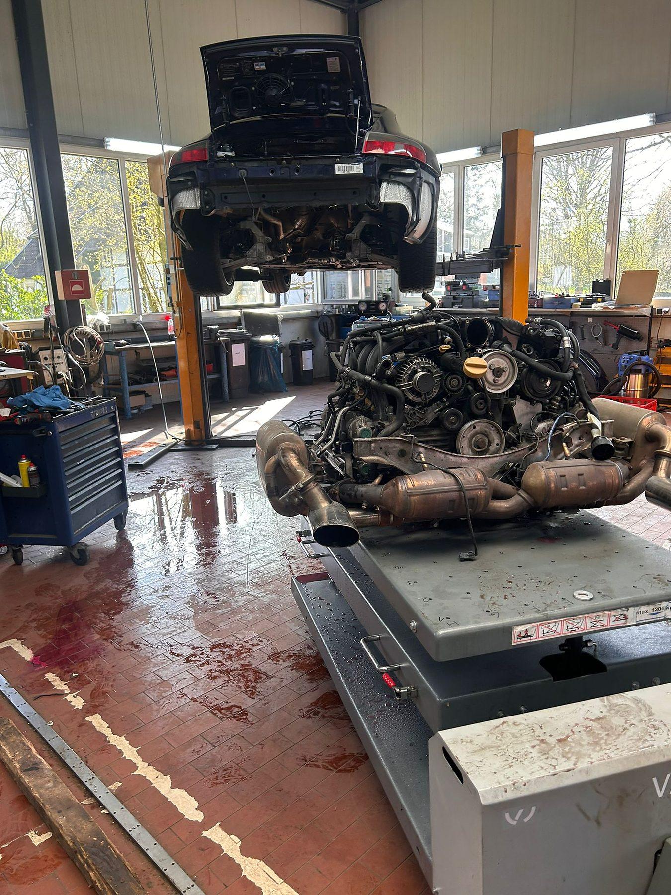 Ausgebauter Motor mit Abgasanlage auf dem Hubtisch unter dem angehobenen Fahrzeug