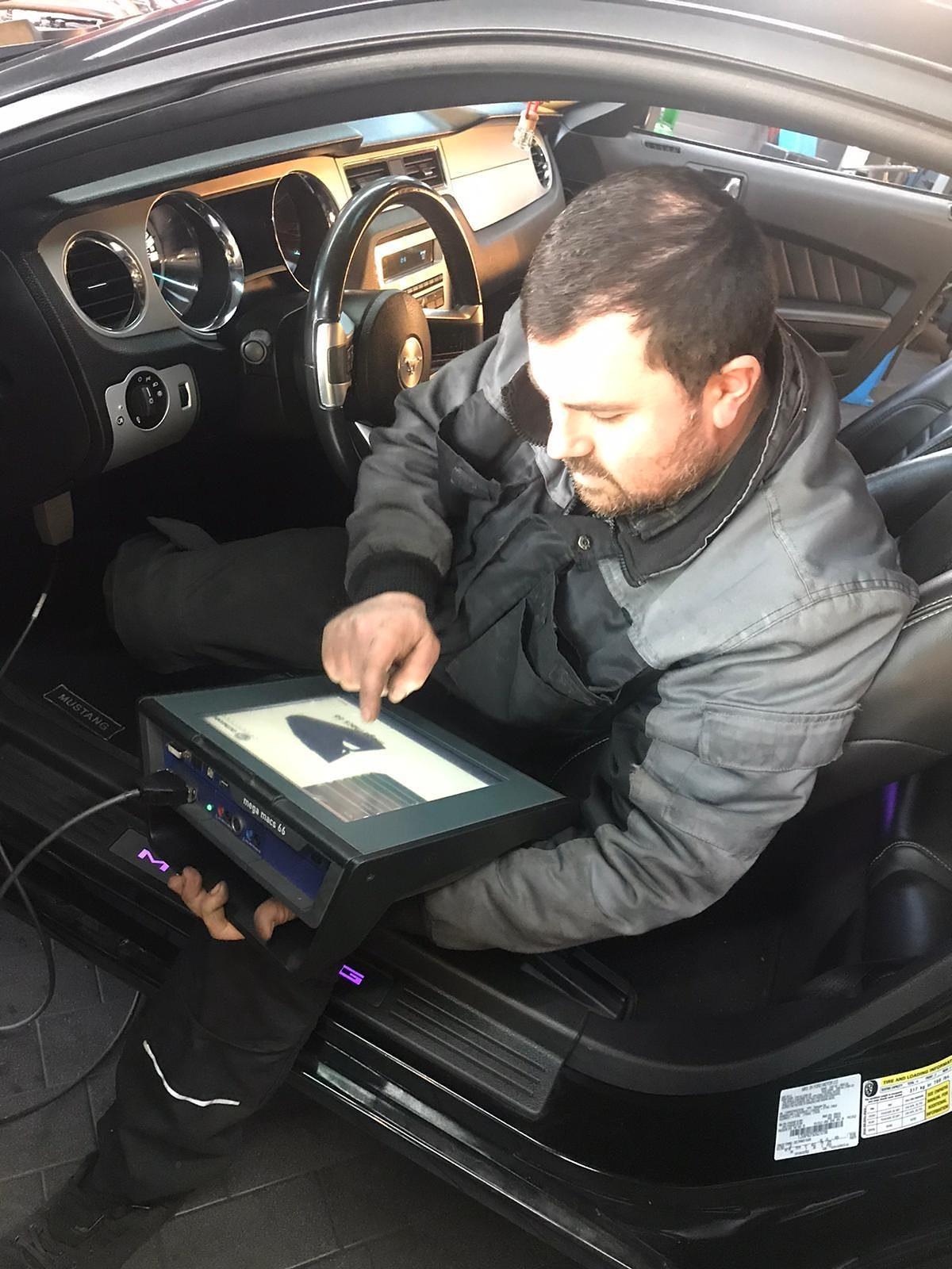 Mechaniker liest im Fahrzeug mit einem Diagnosegerät die Daten aus